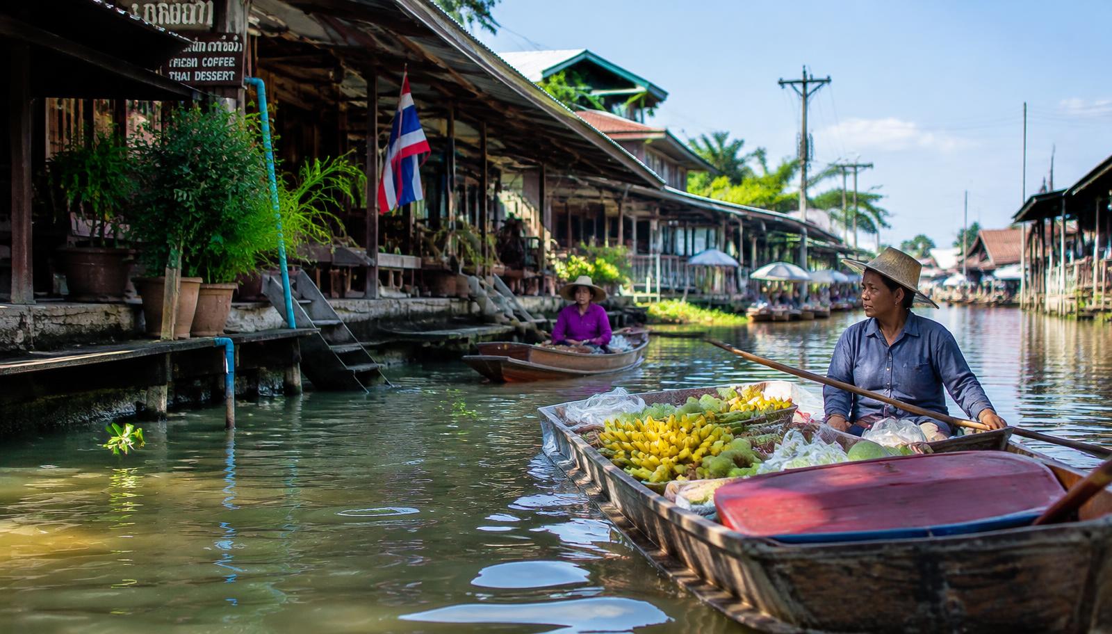 Vendor paddling a wooden boat loaded with bananas and fruit along a canal lined with traditional wooden houses in Bangkok