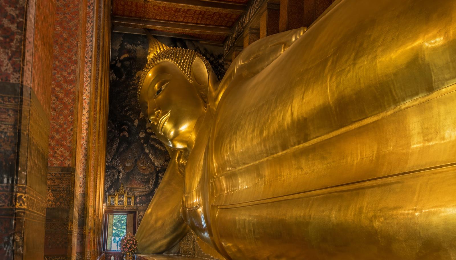 The giant golden Reclining Buddha inside Wat Pho in Bangkok, framed by ornately painted pillars